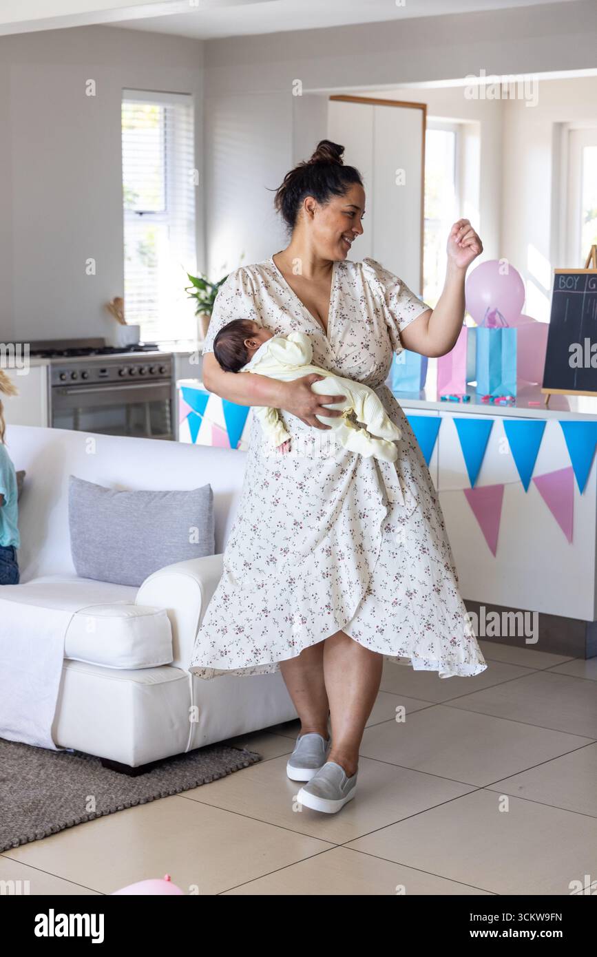 Madre con due bambini che tengono il neonato in braccio e che raggiungono la mongolfiera nel soggiorno accanto alla cucina Foto Stock