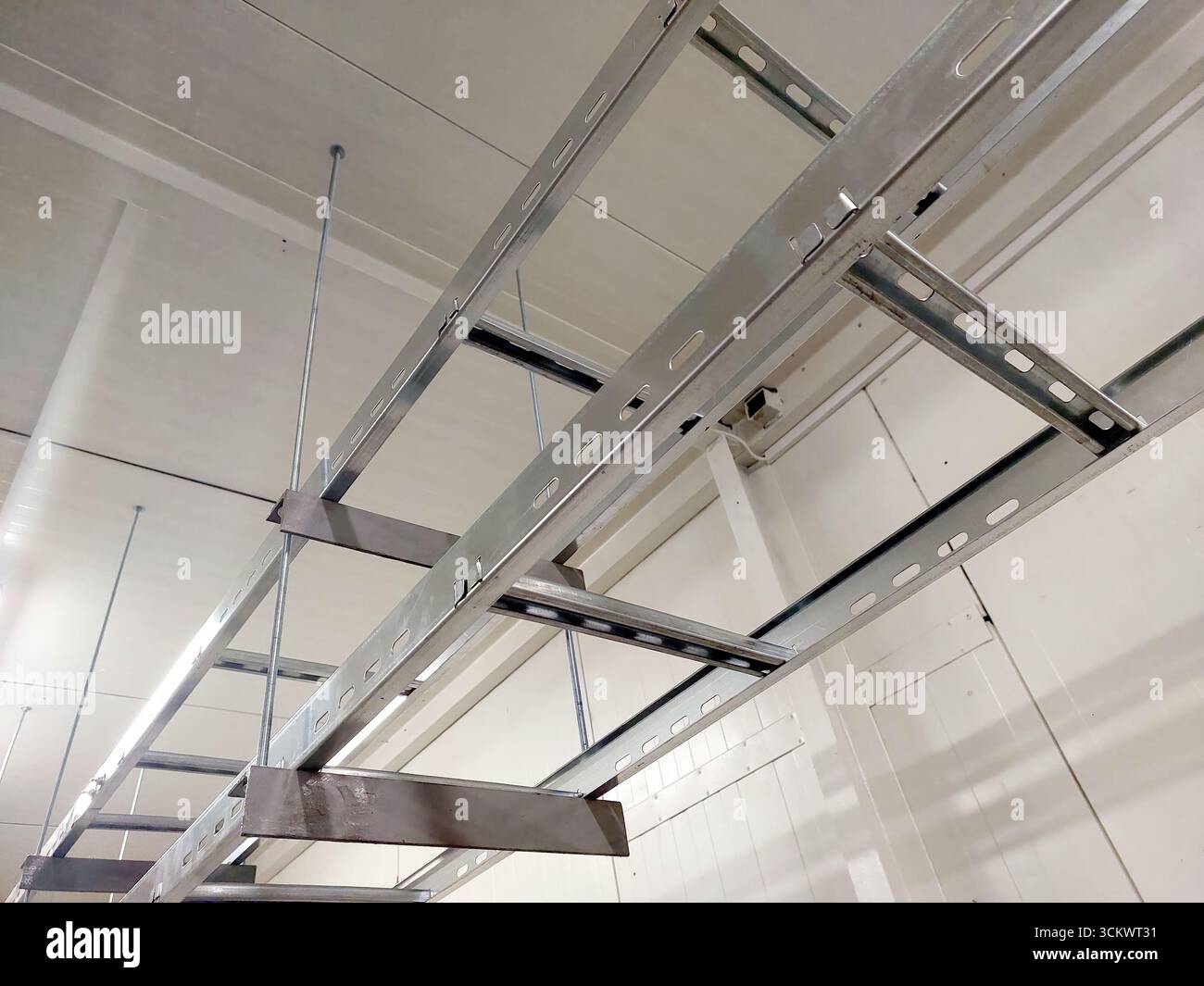 I telai metallici sono appesi al soffitto, fornendo supporto per il cablaggio elettrico in un ambiente industriale ben illuminato. Foto Stock