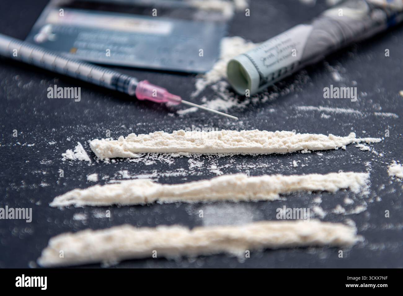 Un'assunzione illegale di droga, concetto di dipendenza con farina bianca divisa in tre file usando una carta di credito, una siringa medica, e un arrotolato 100 US Foto Stock