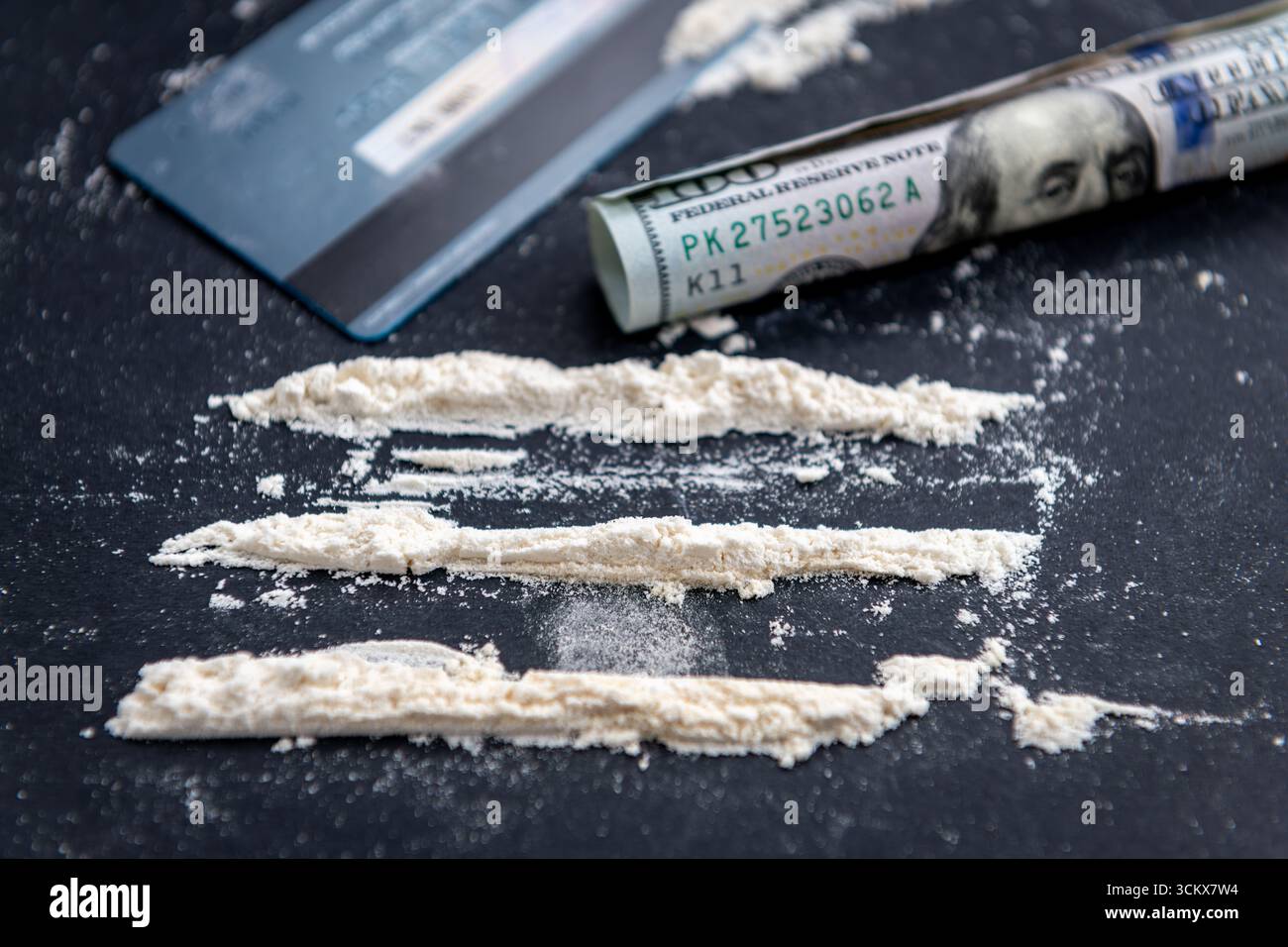 Un concetto di assunzione illecita di droghe, dipendenza con farina bianca divisa in tre file usando una carta di credito, e un isolato di banconota da 100 dollari Foto Stock