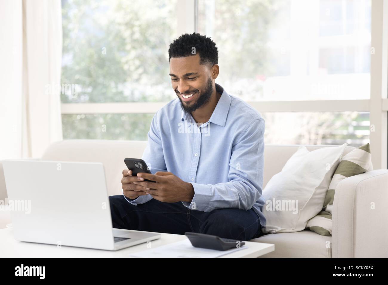 Un giovane sorridente gestisce le finanze personali nel proprio ufficio Foto Stock