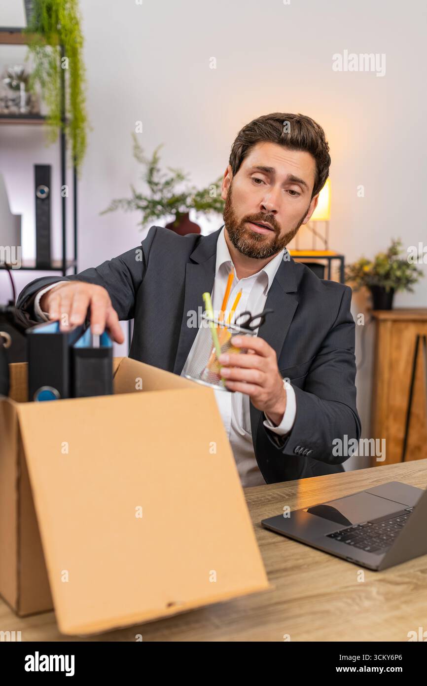 Un uomo d'affari di mezza età in ufficio porta con cura gli oggetti nella scatola e sbircia con nostalgia. Il freelance alla scatola delle etichette del tavolo chiude il notebook e sorride pronto per il prossimo passo in avanti. Foto Stock