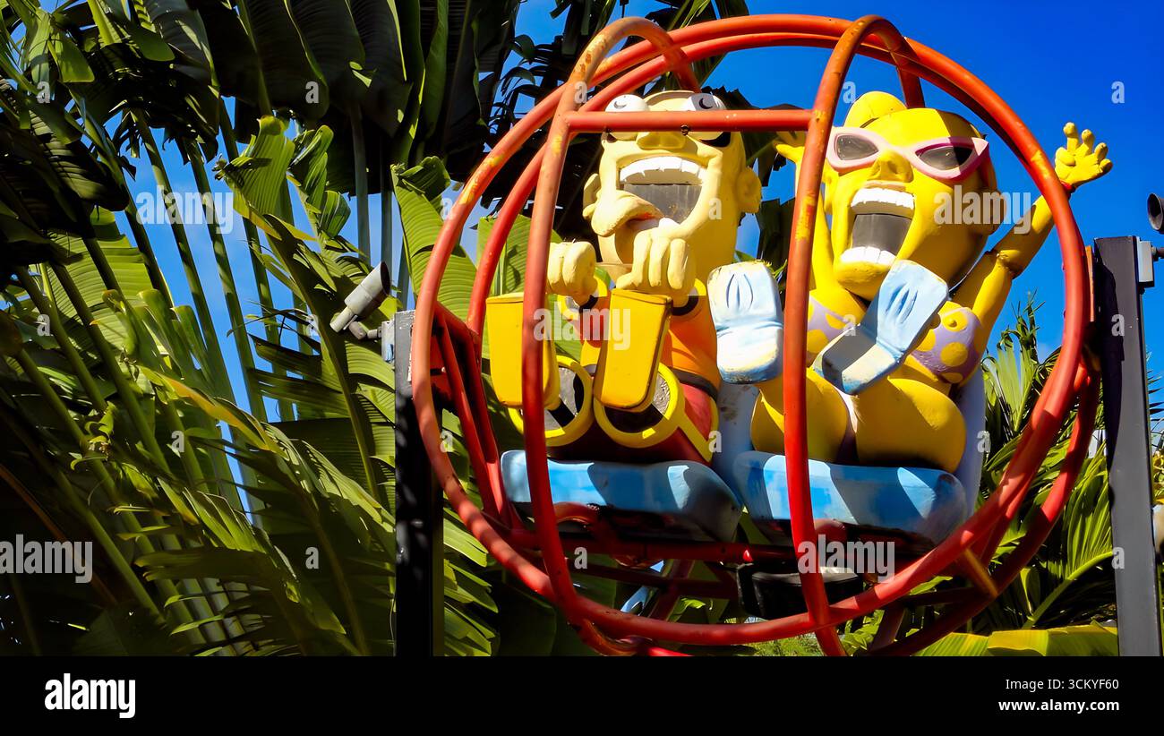 Stravagante scultura di due figure in un giro in Slingshot, che esprime emozioni o paura, sullo sfondo di un parco divertimenti tropicale. Foto Stock