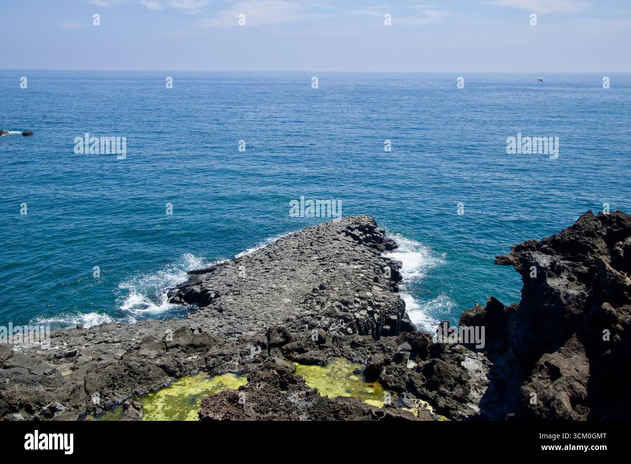 I visitatori si stagliano su un punto panoramico sopraelevato di Daepo Jusangjeolli, sbirciando attraverso aspri affioramenti vulcanici e acque blu che si estendono fino all'orizzonte. Foto Stock