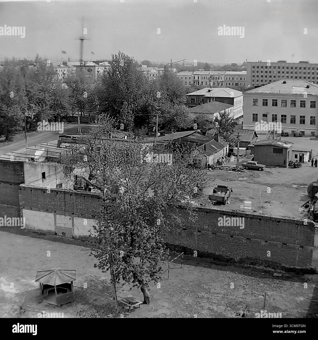 Dietro le quinte di una grande ricostruzione: Vita nei cortili dietro la piazza centrale di Sloviansk, 1975-1976. Lo scatto cattura il caotico mix di vita residenziale, tra cui un parco giochi con gazebo e un'auto sovietica "Zhiguli", continuando nel bel mezzo del grande progetto di rinnovamento della città. Questa fotografia riflette il netto contrasto tra il centro cerimoniale della città e l'autentica vita quotidiana dei suoi abitanti, simboleggiando il mondo pacifico e poliedrico della regione del Donbas, un mondo che esisteva molto prima dei tragici eventi del futuro Foto Stock
