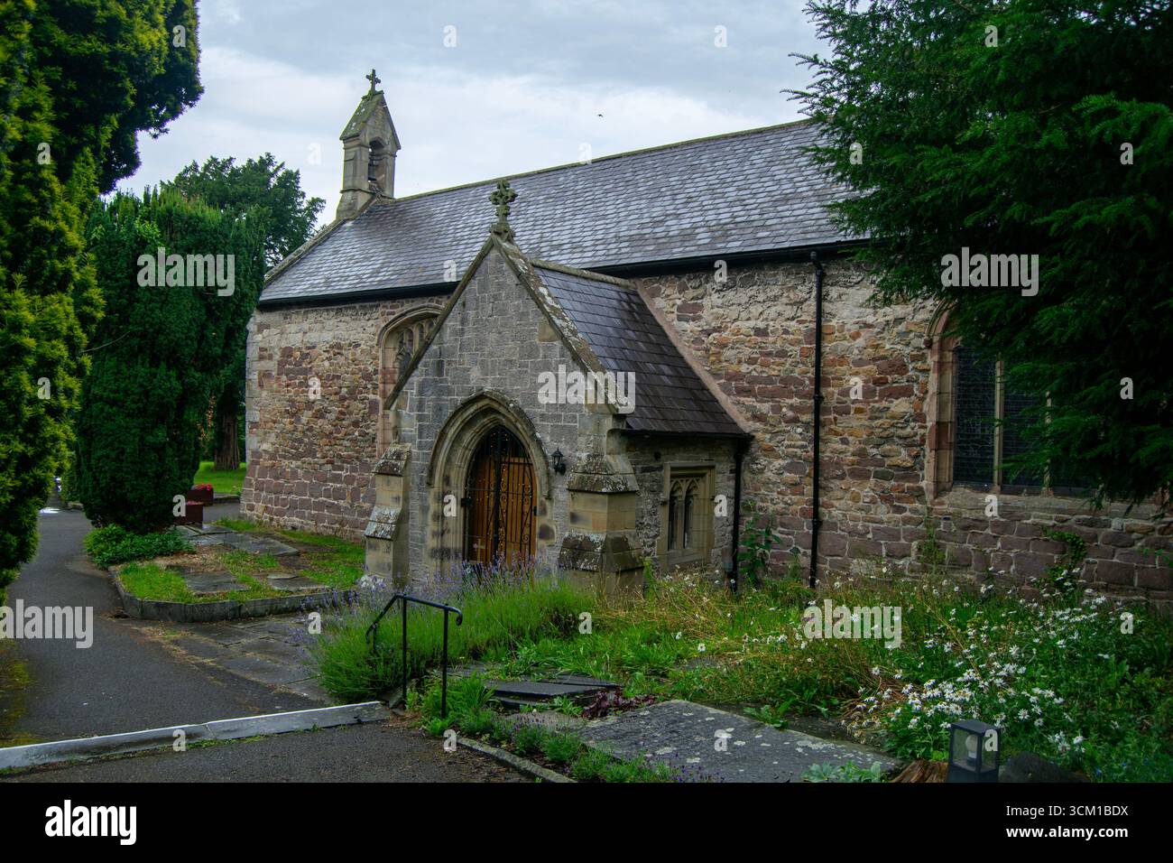 St Asaph Parish Church, Galles. Una vista tranquilla dello storico edificio in pietra e dei suoi terreni, con vegetazione lussureggiante sotto un cielo nuvoloso. Foto Stock
