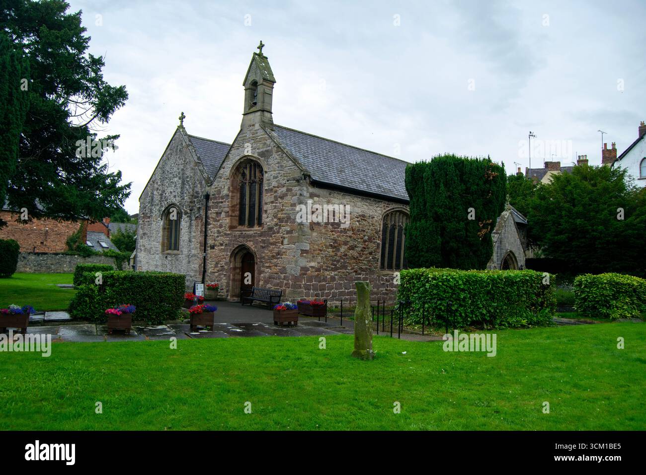 St Asaph Parish Church, Galles. La storica chiesa in pietra con il suo bellcote sorge tra prati verdi e siepi in una giornata nuvolosa. Foto Stock