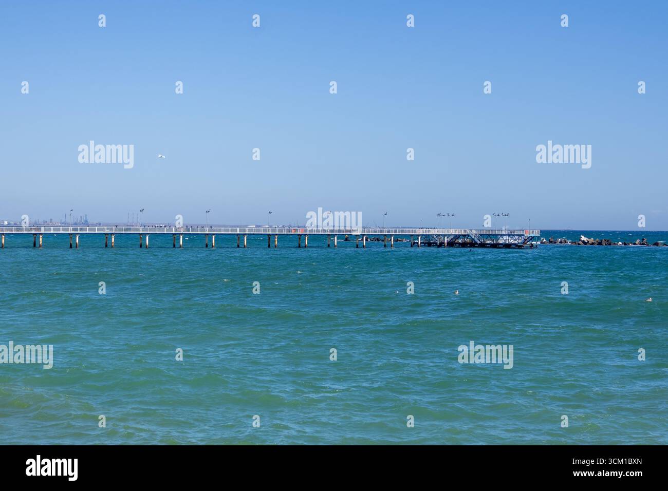 Vista panoramica di un lungo molo che si estende nel mare turchese con un cielo limpido e luminoso. Foto Stock