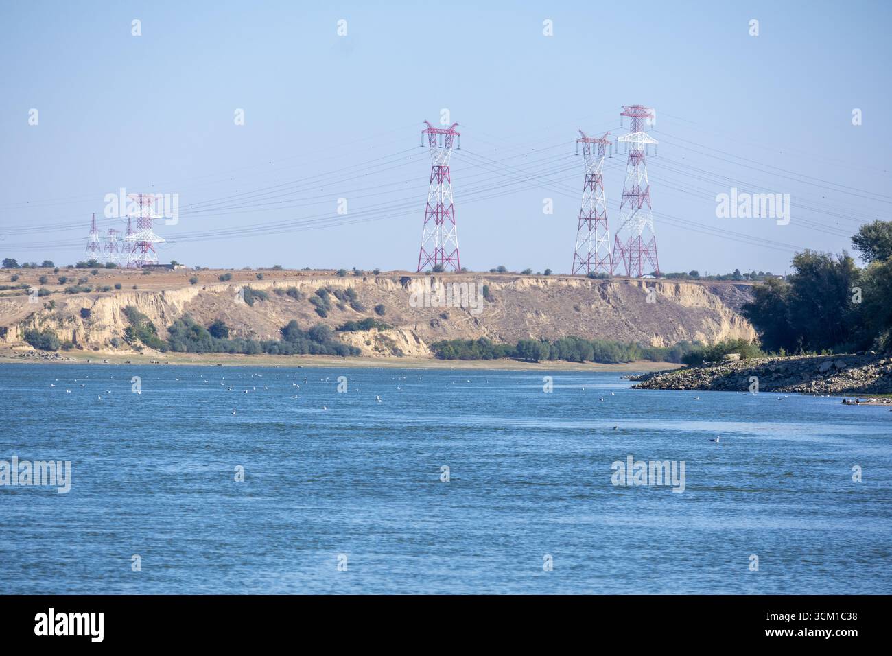 Vista panoramica di un ampio fiume che scorre con alti piloni elettrici e colline sullo sfondo. Foto Stock