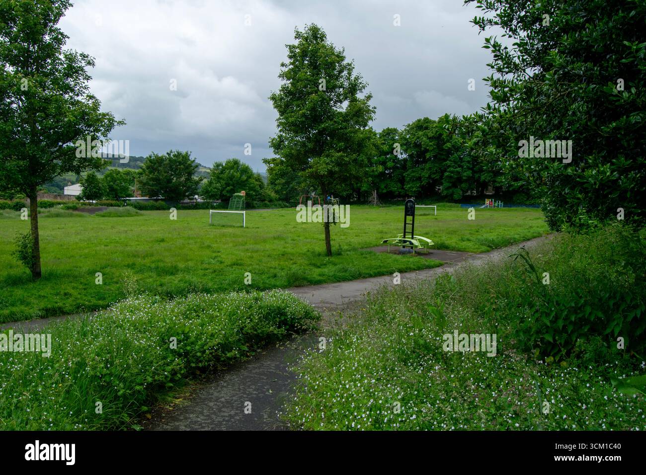 Vegetazione lussureggiante, un sentiero tortuoso e attrezzature da gioco distanti nel panoramico Beech Recreation Ground, Sowerby Bridge, in una giornata coperta. Foto Stock
