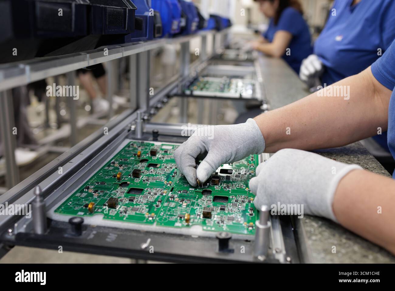 L'operatore colloca i componenti su una scheda a circuito stampato presso una stazione di lavoro ESD su una moderna linea di produzione elettronica in fabbrica Foto Stock