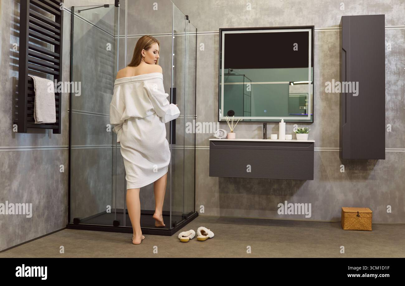 Donna in accappatoio bianco in un bagno moderno con cabina doccia in vetro perfetta Foto Stock