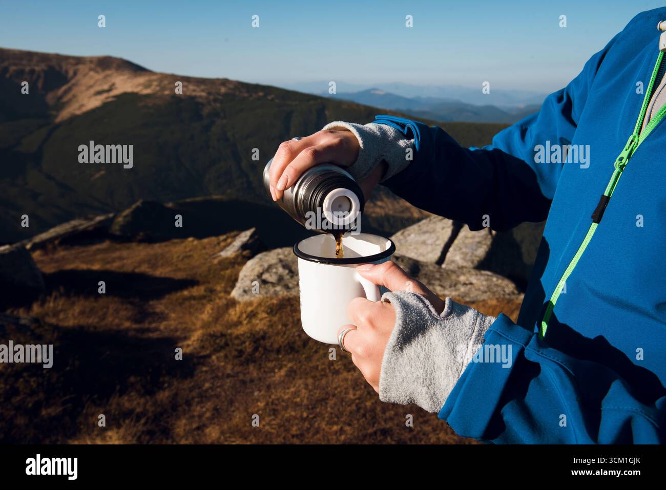 Persona che versa la bevanda calda dal thermos nella tazza sulla montagna. Foto Stock
