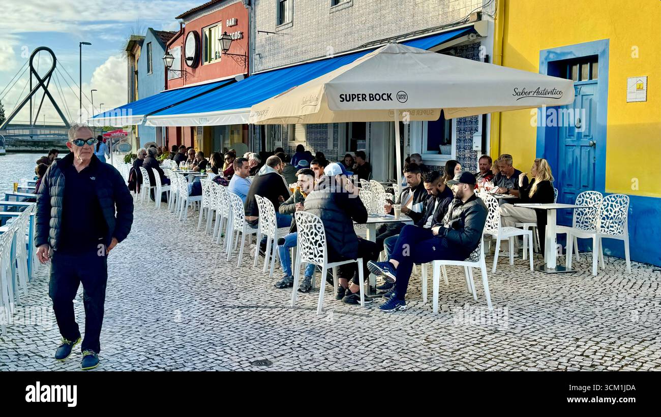 Uomo che cammina davanti a una fila di ristoranti accanto a un canale ad Aveiro in Portogallo - Immagine stock catturata con smartphone