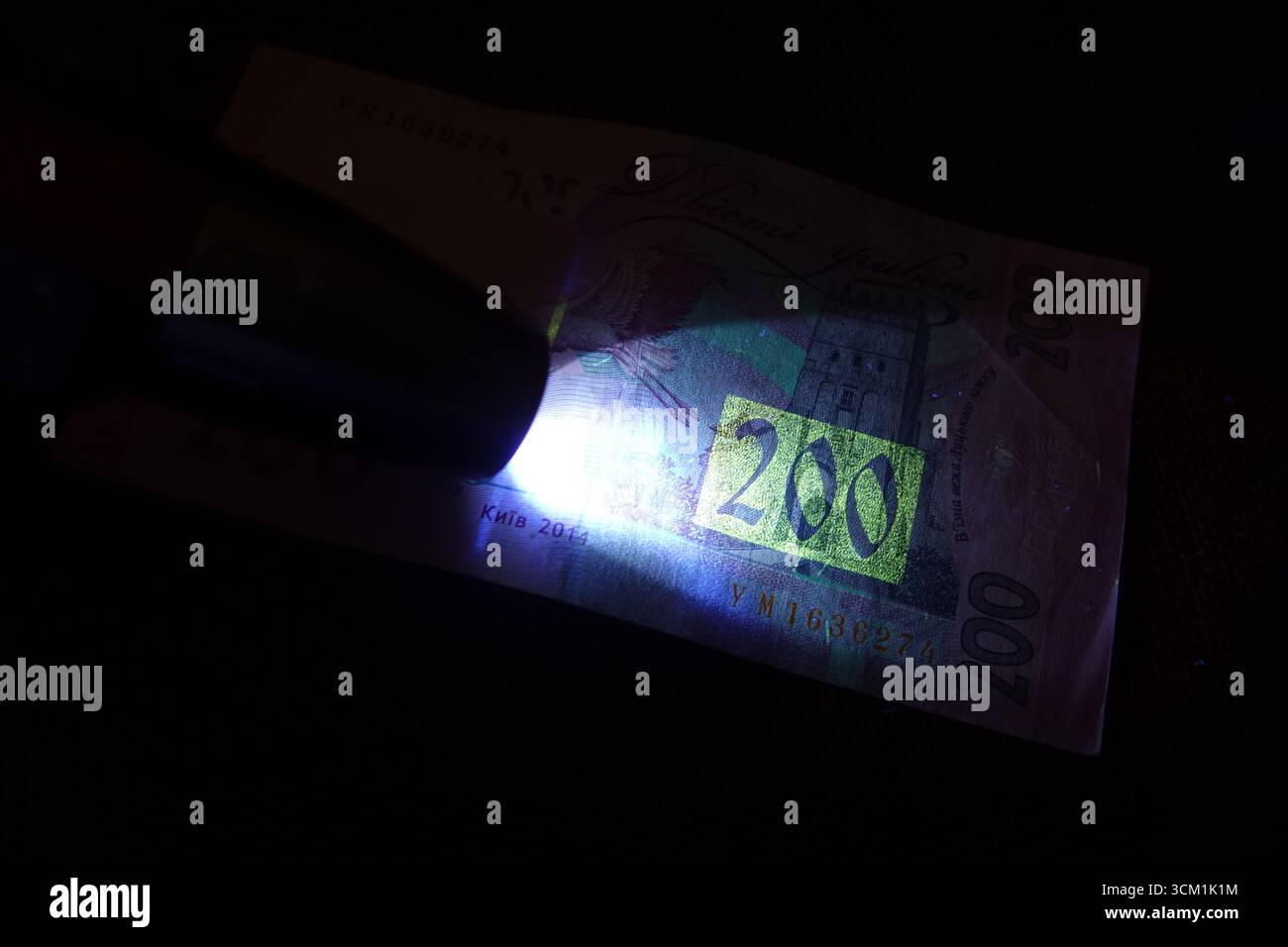 Sotto una luce ultravioletta, vengono esaminate le caratteristiche dettagliate dell'hryvnias Ucraina, mostrando gli intricati segni di sicurezza e la loro vibrante bagliore durante Foto Stock