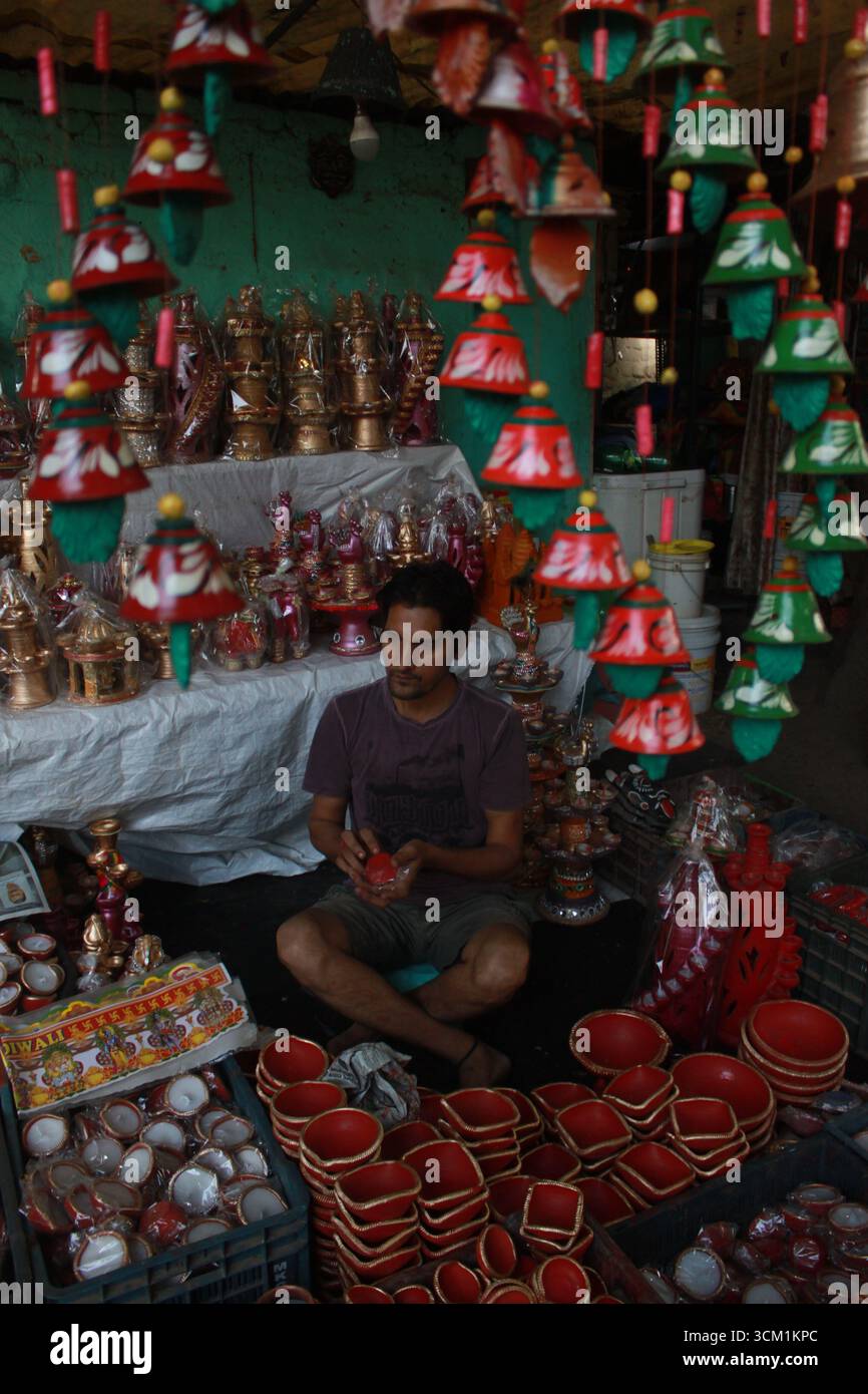 Un negoziante indiano circondato da tutte le cose fatte di argilla - lampade di terra, statuette, lampade a cera e lampade a sospensione a Delhi per Diwali. Foto Stock