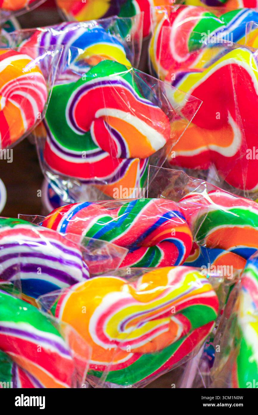 Arcobaleno a forma di cuore e lecca lecca a forma di stella avvolti in plastica. Caramelle colorate e luminose che simboleggiano festeggiamenti, divertimento e dolcetti natalizi. Foto Stock