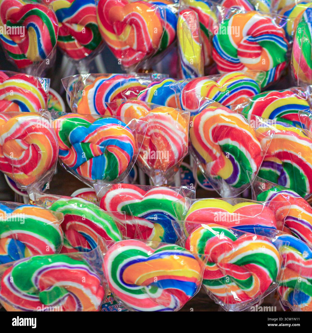 Lecca arcobaleno a forma di cuore e rotonda, avvolti in plastica. Caramelle colorate che simboleggiano il divertimento dell'infanzia, le feste e le prelibatezze natalizie. Foto Stock