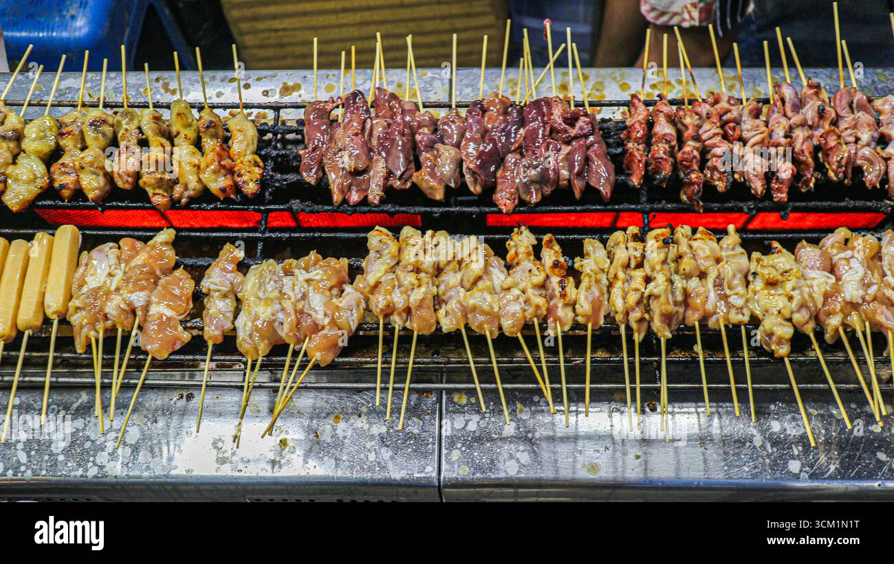 Spiedini tailandesi di maiale, intestino di pollo e salsiccia grigliata su carbone. Autentico stile Street food con sapore affumicato e tradizione culinaria locale. Foto Stock
