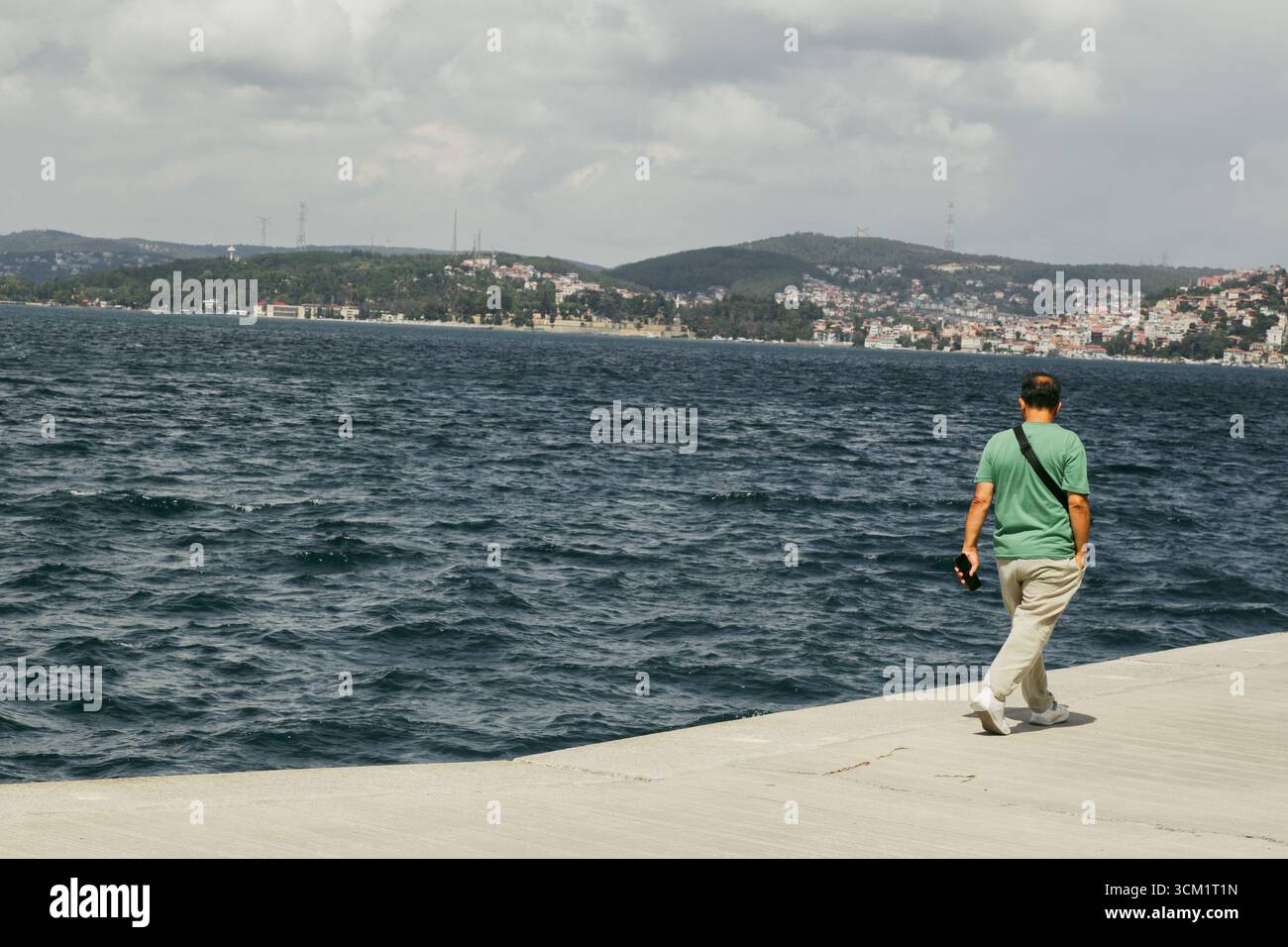 Uomo in camicia verde cammina lungo lo stretto del bosforo a Istanbul Foto Stock