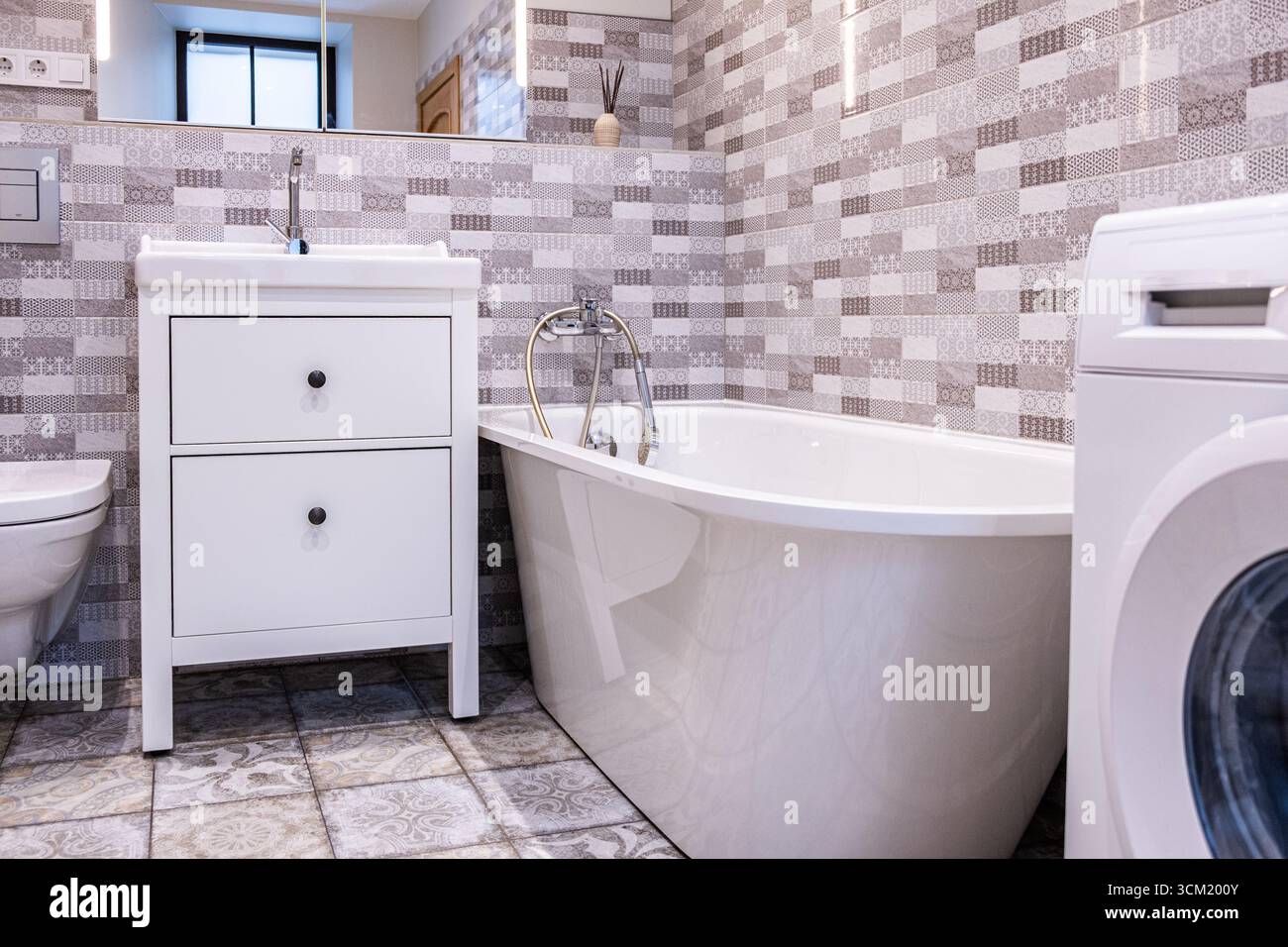 Il bagno contemporaneo presenta un'elegante vasca bianca, un elegante ripostiglio e piastrelle a motivi geometrici, sottolineando un design funzionale e spazioso con AM Foto Stock
