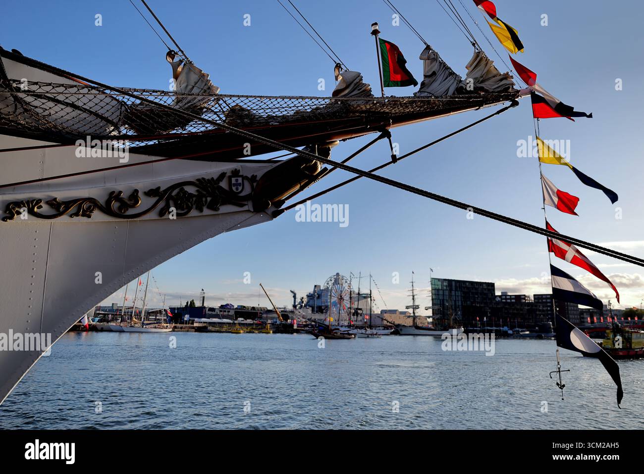Dettaglio di un veliero con armatura, bunting e insegna, fotografato al Sail 2025 di Amsterdam, Paesi Bassi, affacciato sull'acqua del porto. Foto Stock