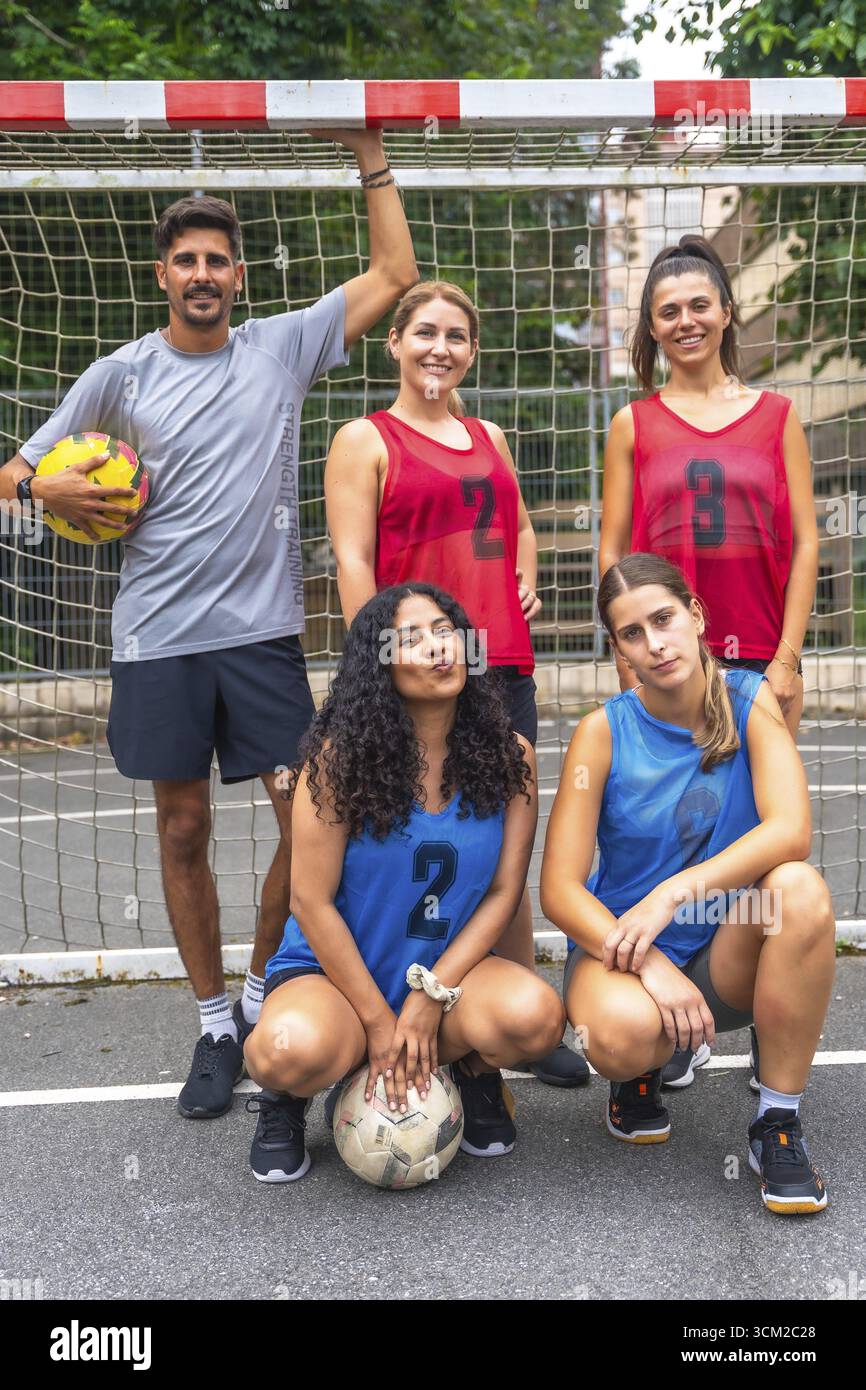 Cinque giovani giocatori di calcio, che indossano maglie numerate, stanno posando per una foto della squadra su un campo all'aperto, tenendo le palle da calcio e stando in piedi davanti a loro Foto Stock