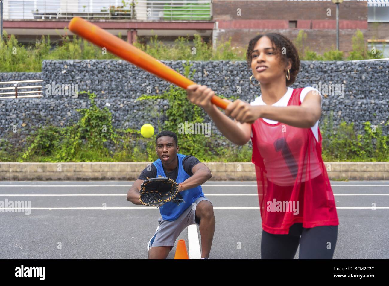 Giocatrice di baseball che fa oscillare una mazza per colpire una palla mentre un ricevitore maschio si prepara a prenderla. Momenti ricchi di azione che catturano l'emozione del ga Foto Stock