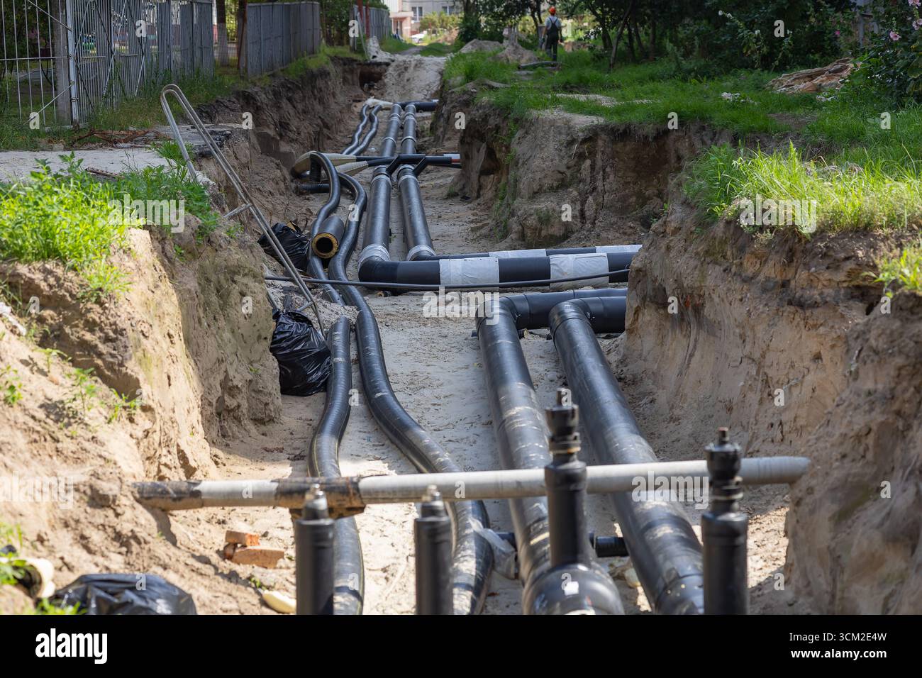 Cantiere urbano con grandi tubi dell'acqua neri disposti in una trincea durante la riparazione e la sostituzione delle infrastrutture cittadine Foto Stock