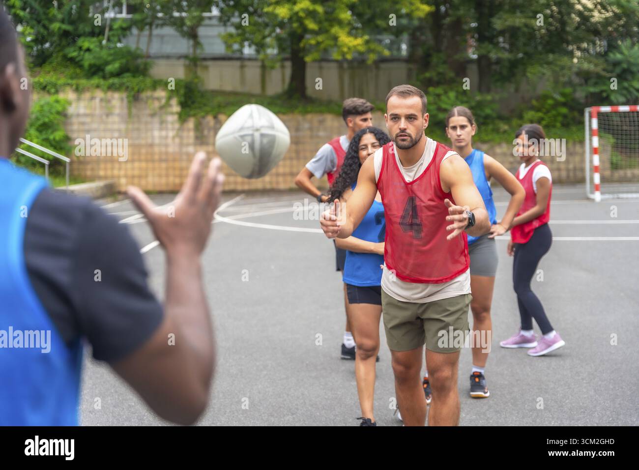 Giocatori di rugby multietnici impegnati in esercitazioni di passaggio su un campo all'aperto all'interno di un parco cittadino, promuovendo il lavoro di squadra, promuovendo il fitness e dimostrando Foto Stock