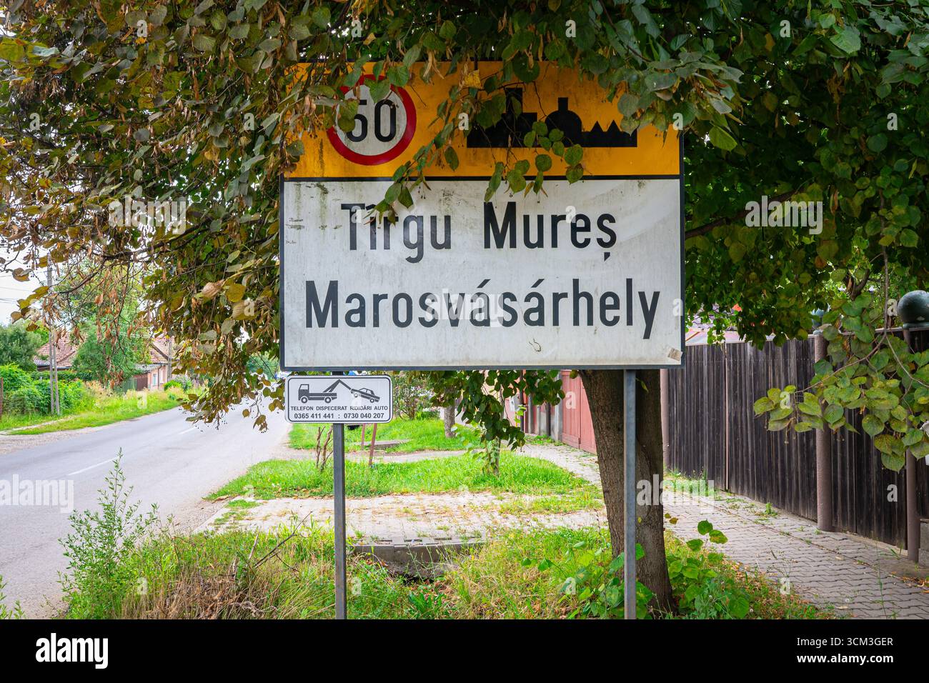 Cartello stradale bilingue che mostra Tirgu Mureș e Marosvásárhely in Romania, circondato da lussureggianti vegetazioni. Foto Stock