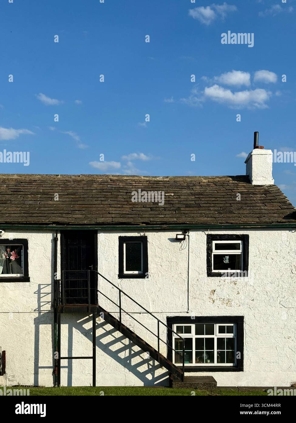 Pub imbiancato con finestre delineate in nero e all'ombra delle scale contro un cielo blu. Black Lanes End Tavern, Colne Lancashire - Immagine stock catturata con smartphone