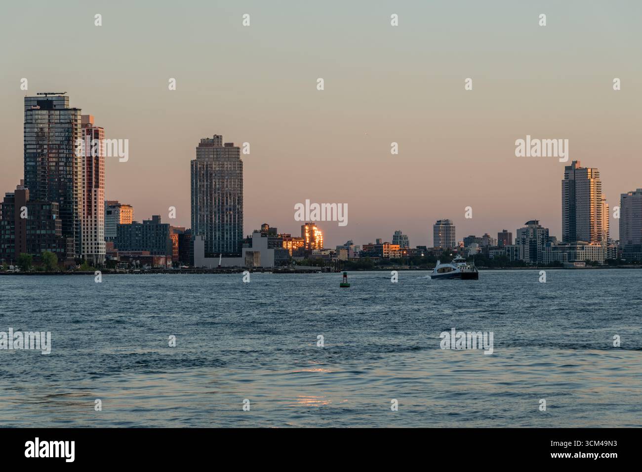 Il sole si riflette nelle finestre dell'edificio al tramonto a Brooklyn lungo la riva dell'East River, vista dall'altra parte del fiume a Manhattan, New York City Foto Stock