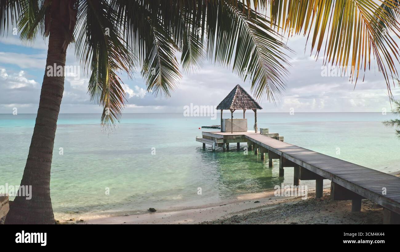 Polinesia francese, isola di Rangiroa: Incorniciata da splendidi paesaggi marini. Le foglie di palma circondano un molo di legno che conduce ad un bungalow sull'acqua. Un tranquillo gazebo sul lungomare in legno. Posizione idilliaca tropicale Foto Stock
