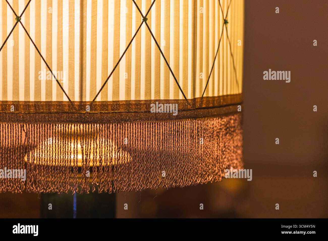 Elegante paralume in tessuto vintage con frange ornamentali e design classico a righe. Illuminato con calore, trasuda un'atmosfera intima e nostalgica perfetta Foto Stock