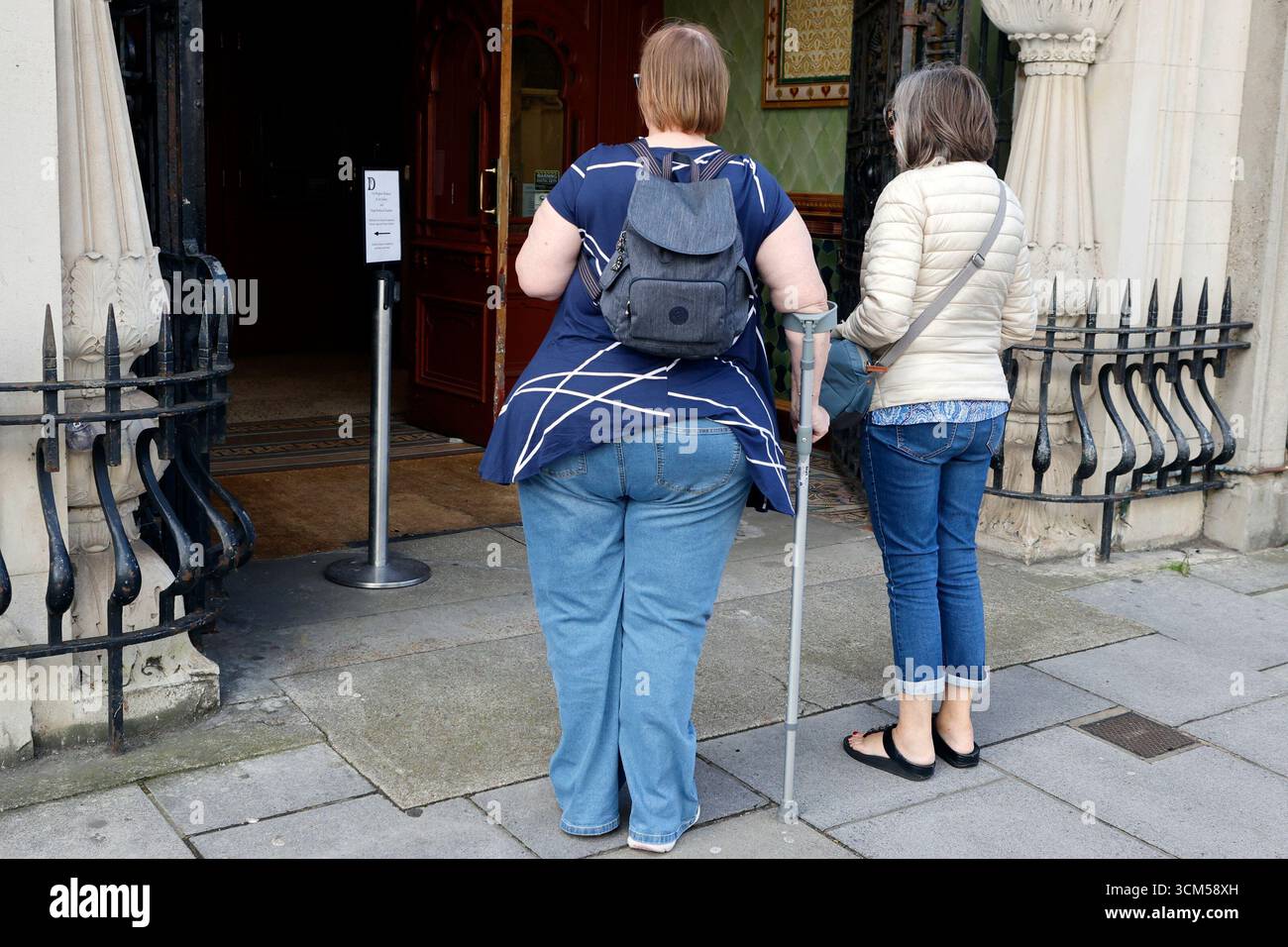 Donna in sovrappeso con una stampella per aiutare a camminare Foto Stock