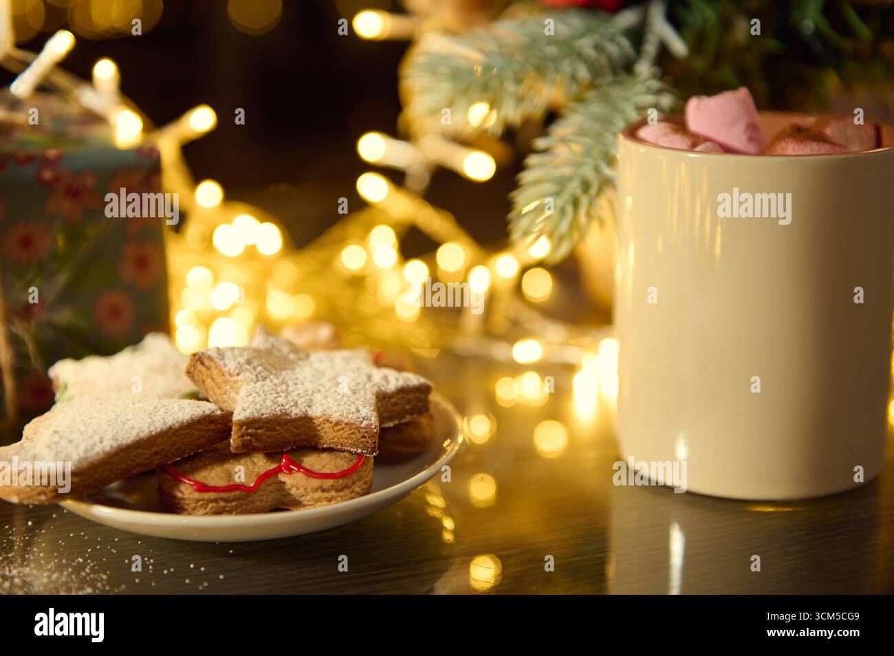 Atmosfera festosa con biscotti a forma di stella spolverati con zucchero, una tazza calda di cacao adornata con marshmallow e luci decorative che creano un caldo caldo ambiente Foto Stock