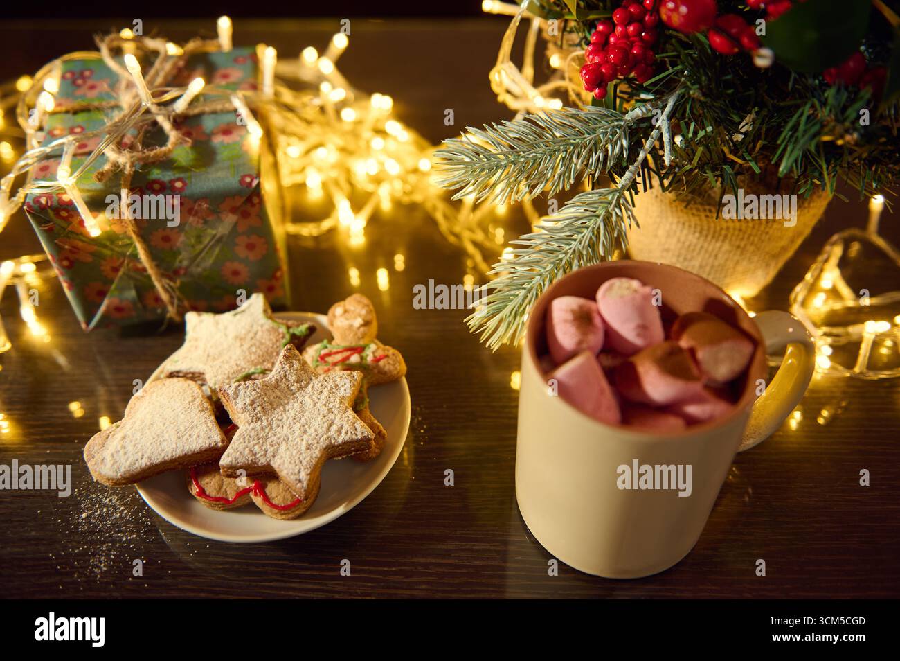 Un ambiente accogliente per le vacanze con biscotti natalizi a forma di stella, una tazza di cioccolata calda con marshmallow e ornamenti natalizi splendidamente disposti Foto Stock