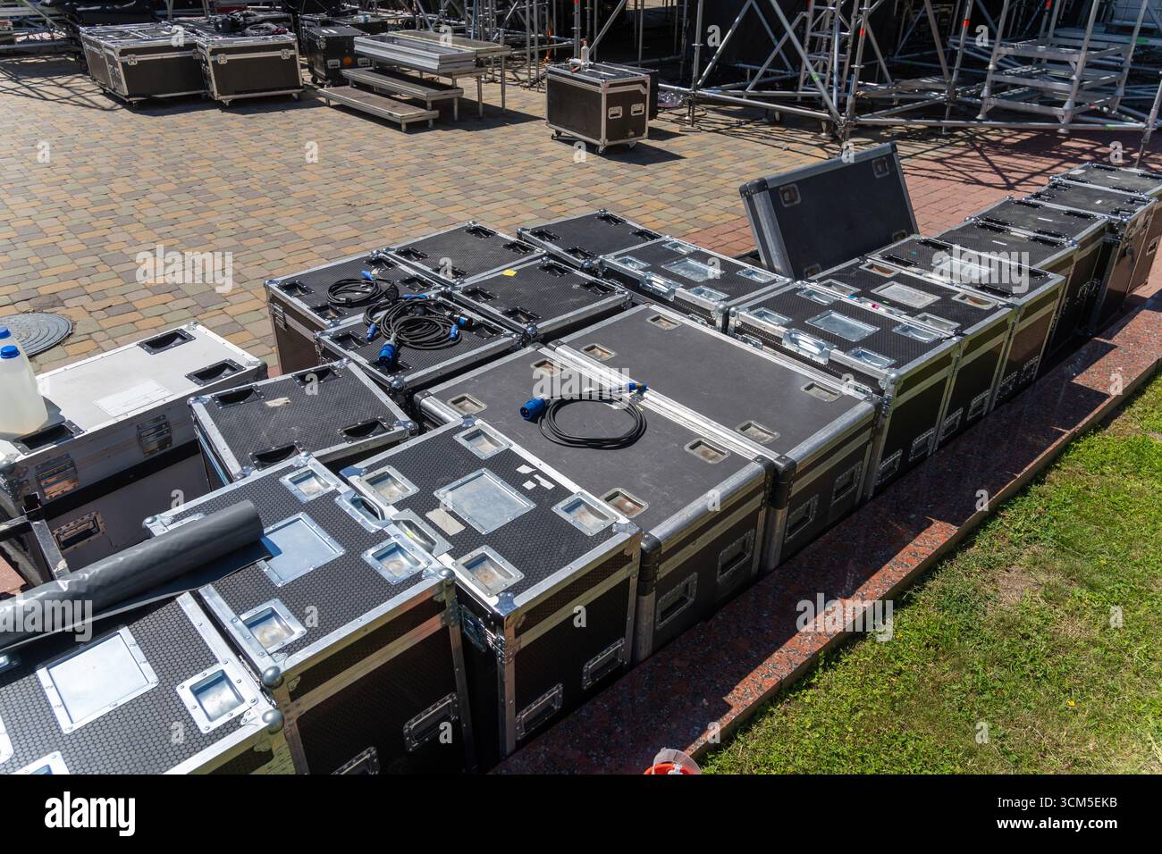 Scatole con apparecchiature audio e di illuminazione e cavi vicino a un palco da concerto durante l'installazione. Preparatevi per un programma musicale all'aperto con attrezzature audio professionali Foto Stock