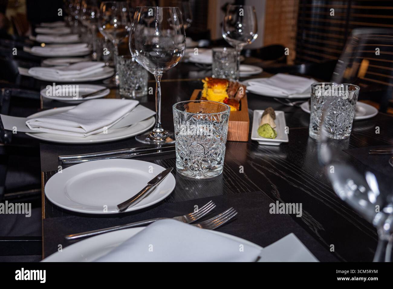 Sofisticato ambiente da tavolo in un ristorante, con bicchieri di cristallo, piatti bianchi e tovaglioli ben disposti, a creare un ambiente elegante per Foto Stock