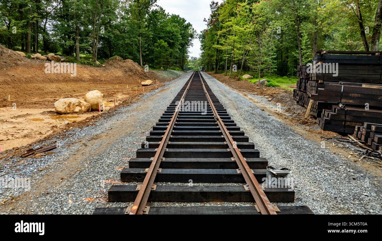 I lavoratori stanno costruendo una nuova linea ferroviaria con cravatte appena posate e ghiaia, circondata da alberi in un paesaggio sereno in autunno. Il progetto ai Foto Stock