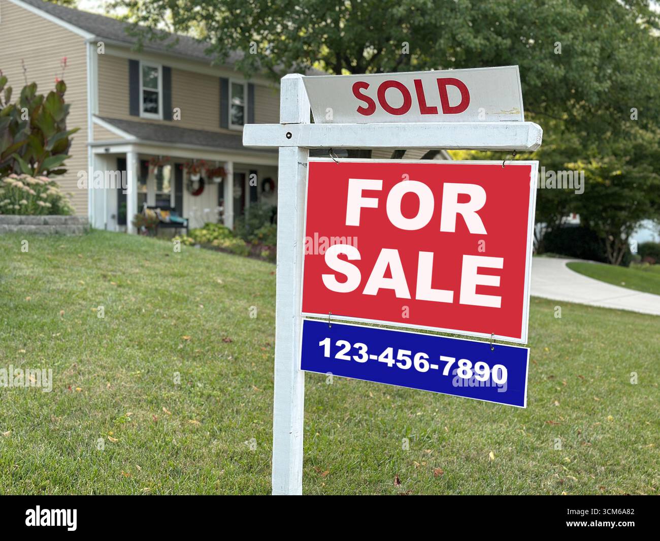 Una casa residenziale con un cartello in vendita contrassegnato come venduto nel cortile anteriore. Il segno rosso e bianco con un numero di telefono rappresenta le transazioni immobiliari, l'acquisto di abitazioni e la vendita di immobili. Foto Stock