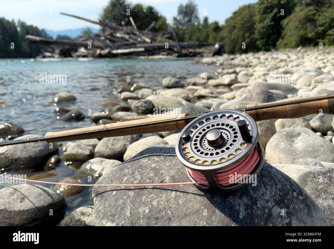 Primo piano di un mulinello per la pesca con la mosca e di un'attrezzatura per canne su una grande roccia con il fiume Skagit e un ingorgo di tronchi sullo sfondo. Situato nello stato di Washington durante la tarda notte Foto Stock