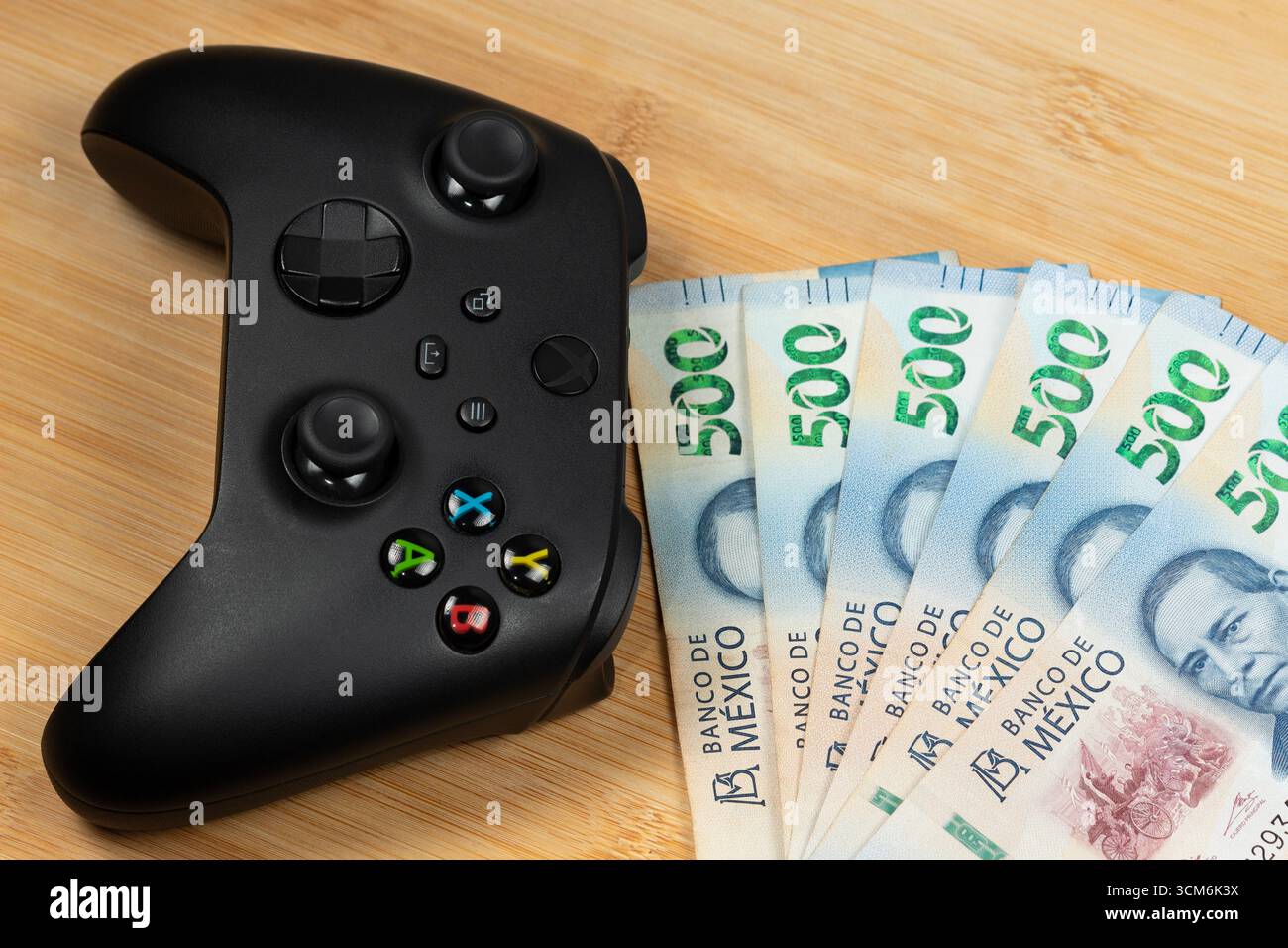 Foto macro su un controller nero xbox One vicino a banconote messicane su uno sfondo di legno Foto Stock