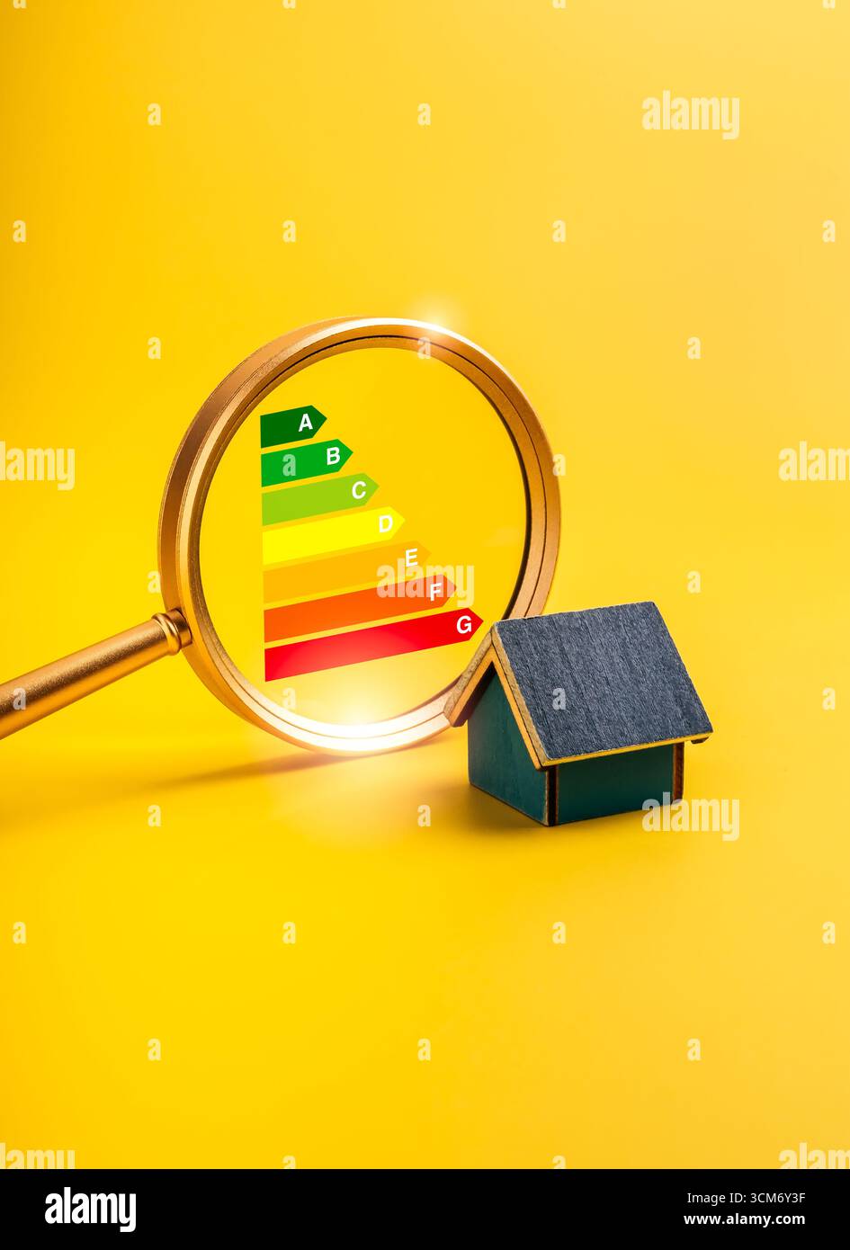 Concetto di casa a risparmio energetico con lente di ingrandimento focalizzata su scala di valutazione colorata e modello di casa in legno di piccole dimensioni, simbolo di un architetto ecologico Foto Stock