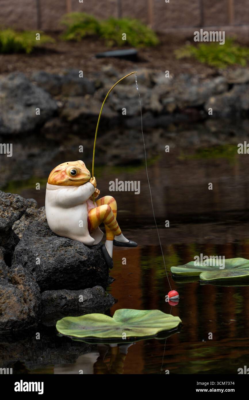 Una stravagante statuina di rana che pesca in uno stagno presso l'area di osservazione del Fuji Shibazakura Festival, Lake Motosu Resort, Prefettura di Yamanashi, Giappone. Foto Stock