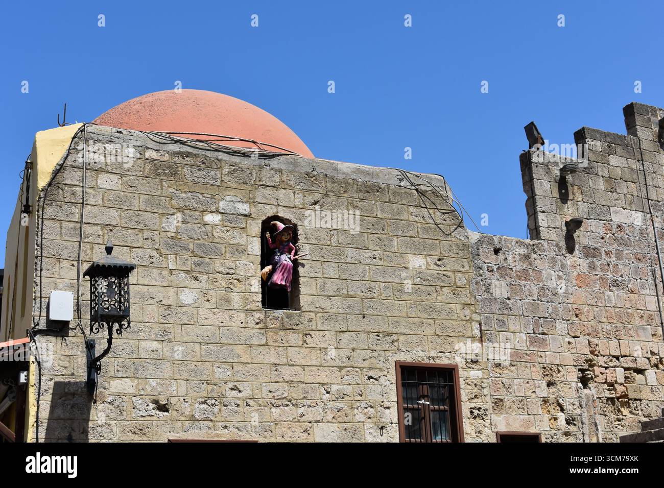 Strega su una scopa nella finestra di un edificio storico in piazza Ippocrate a Rodi, Grecia. Palazzo Castellania con Biblioteca pubblica centrale Foto Stock