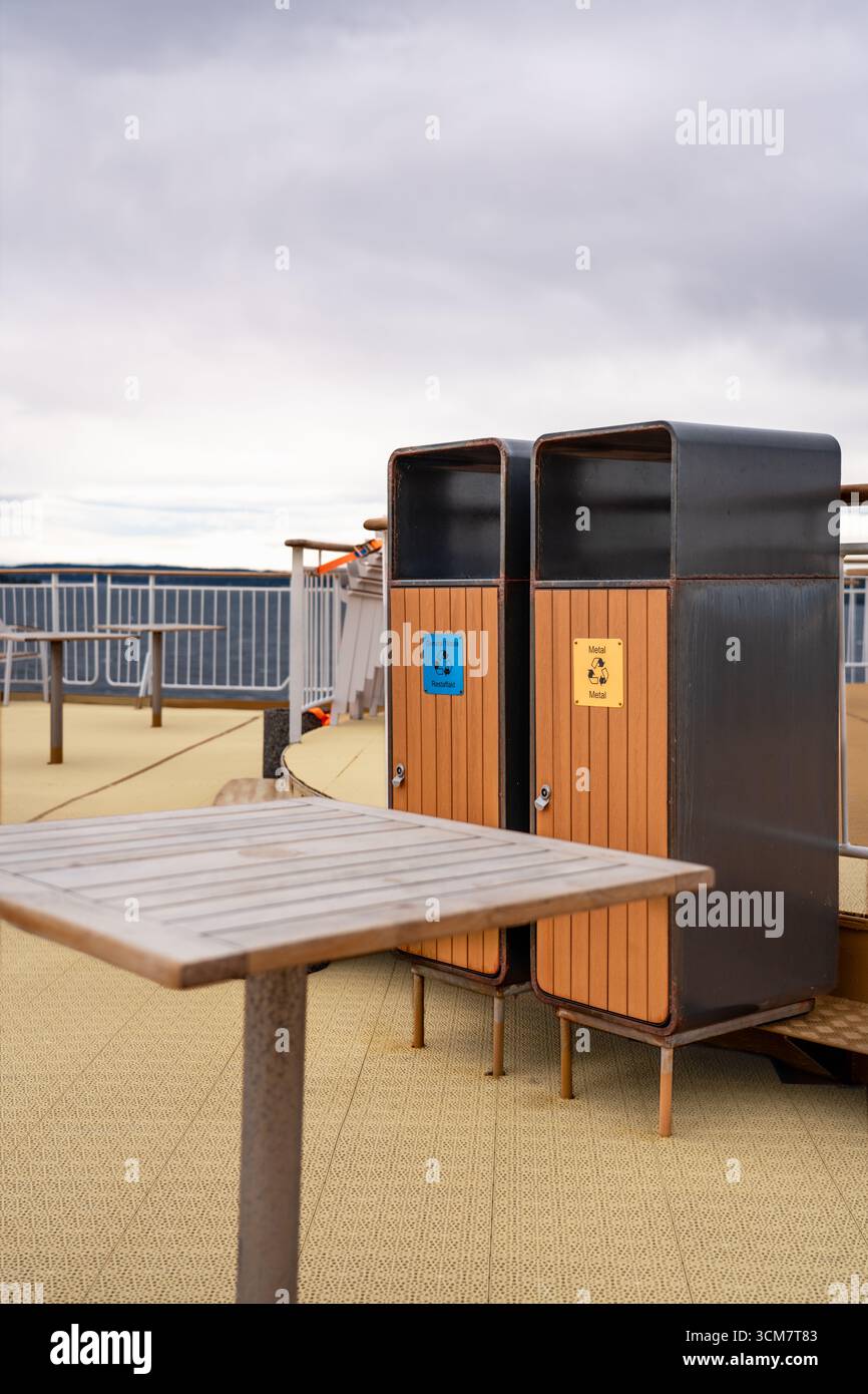 Due contenitori per rifiuti per il riciclo dei residui e dei metalli si trovano sul ponte posteriore di una nave da crociera, evidenziando l'ambiente pulito e organizzato Foto Stock