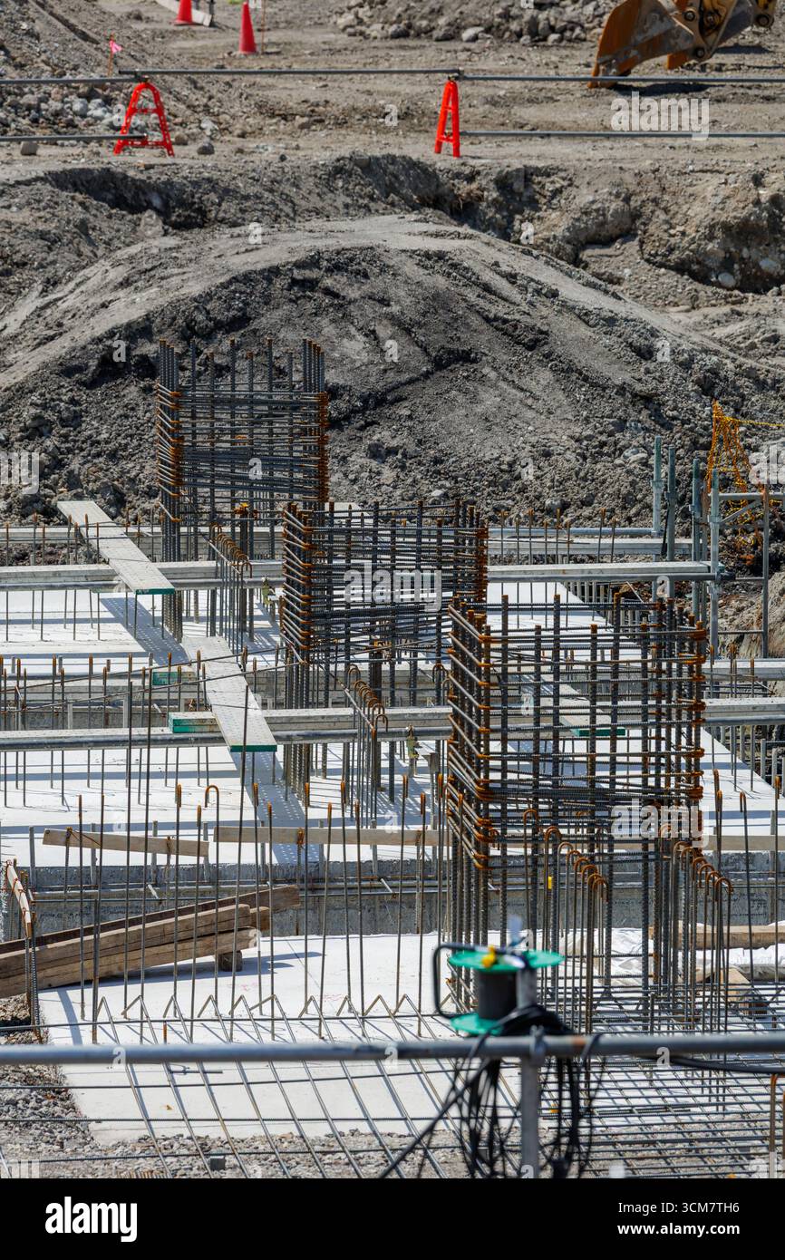 I rinforzi in acciaio risalgono dalle fondamenta in calcestruzzo del cantiere. Vari strumenti e materiali sparsi nell'area indicano il lavoro in corso. Foto Stock