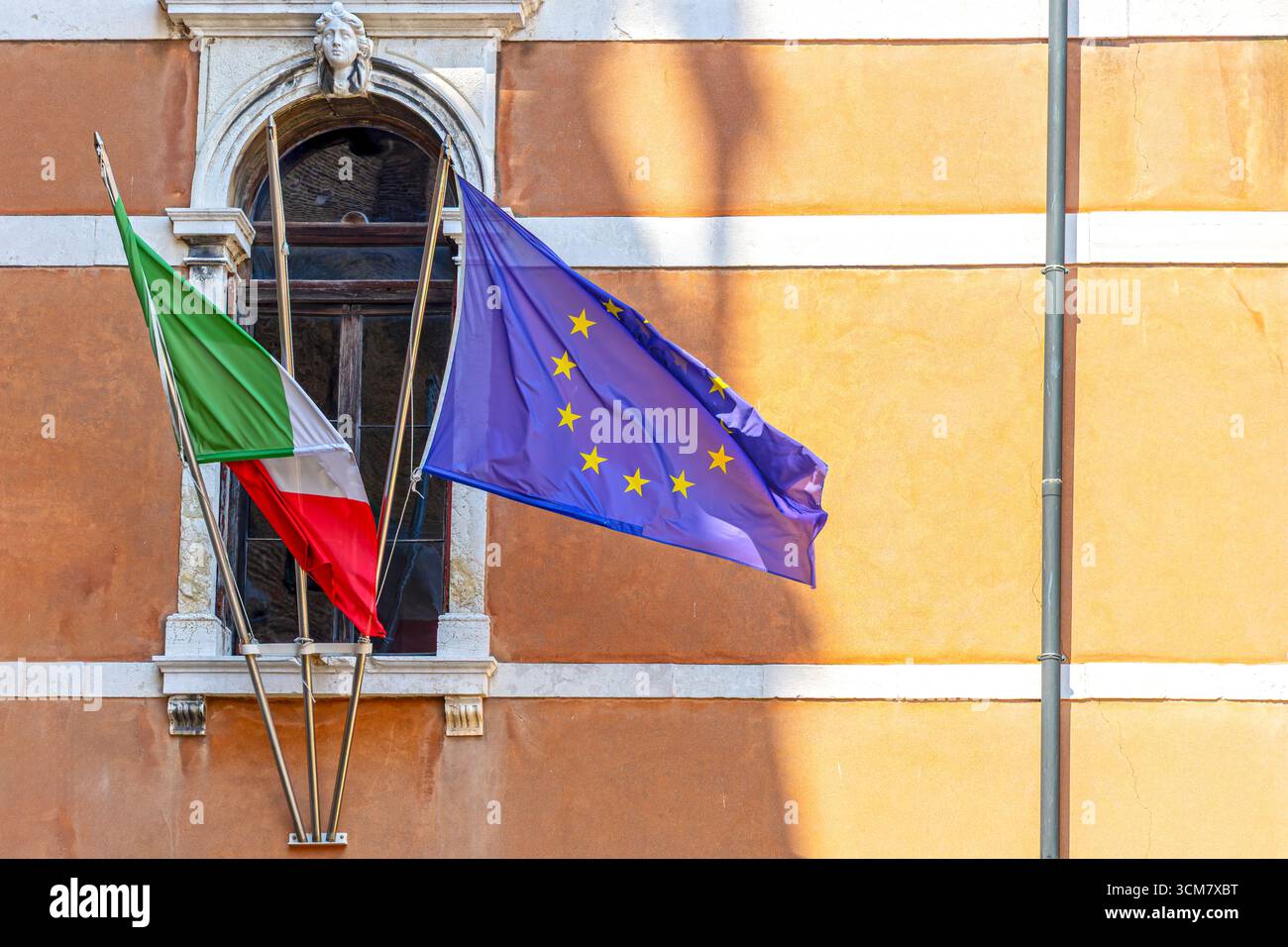 Unione europea e bandiere italiane sugli edifici. Primo piano delle bandiere dell'Unione europea e italiane che sventolano fuori da un vecchio edificio con una finestra decorativa e. Foto Stock